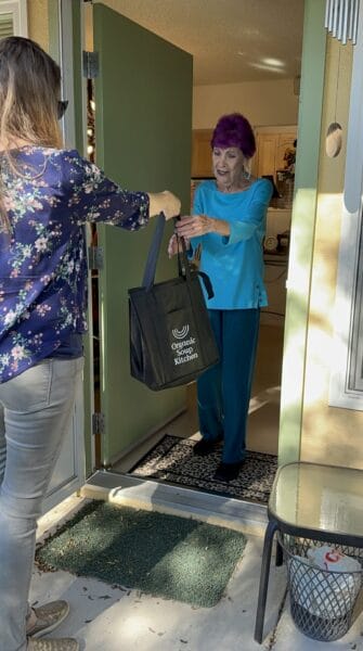 Picture of a person handing an Organic Soup Kitchen bag to another person at a front door